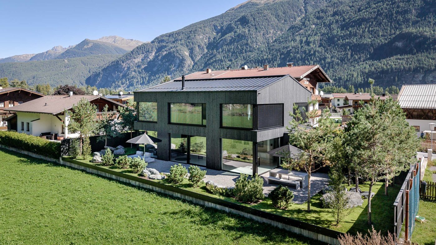Schwarzes Holzhaus mit Garten und Terrasse vor den Bergen des Ötztals
